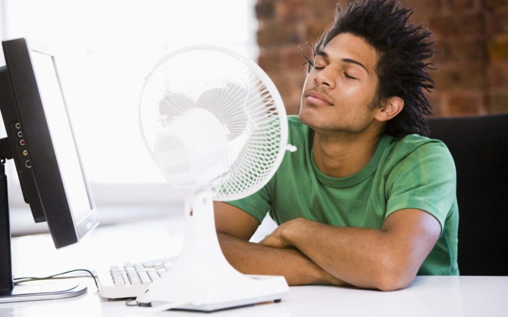 Man sitting in front of a fan because he needs a new air conditioner.