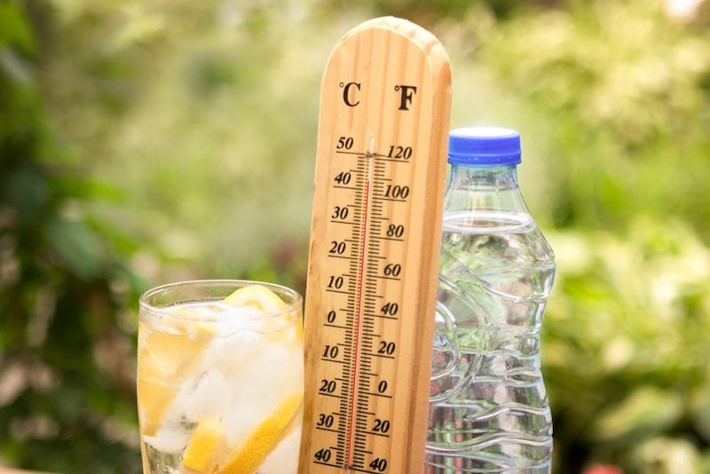 A glass of lemonade, a water bottle, and a thermometer showing the hot summer temps show why it's important for AC to work.