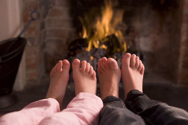 Children's feet warming at a fireplace sitting down in living room.