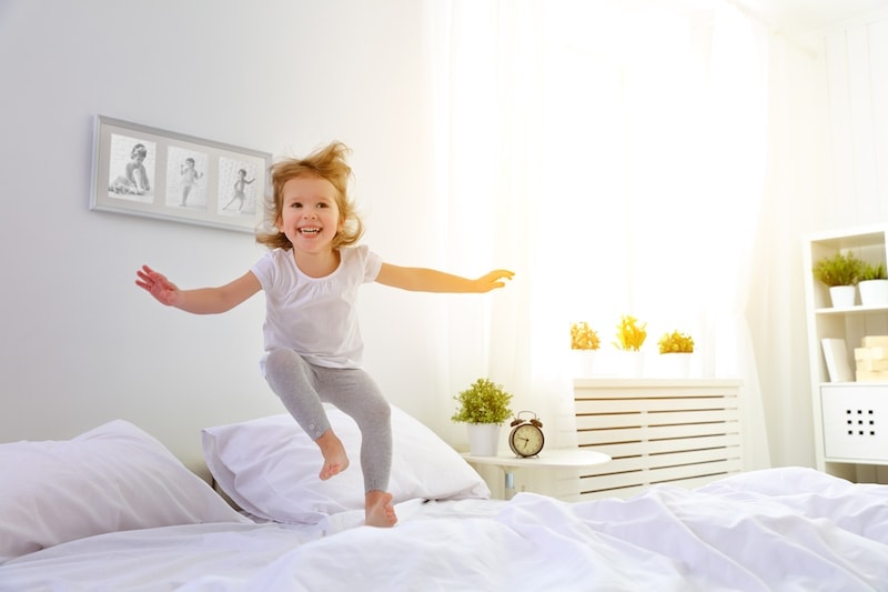 Little girl jumping on a white bed.