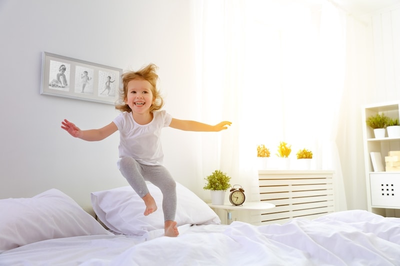 little girl jumping on a white bed.