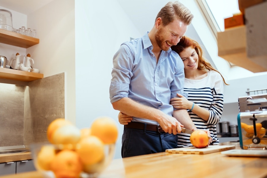 A man and wife cutting a squash on a cutting board.