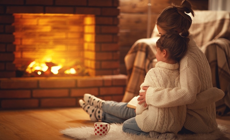 Mother and daughter cuddling by the fire.