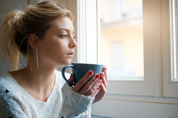 Woman holding a mug of tea by the window.