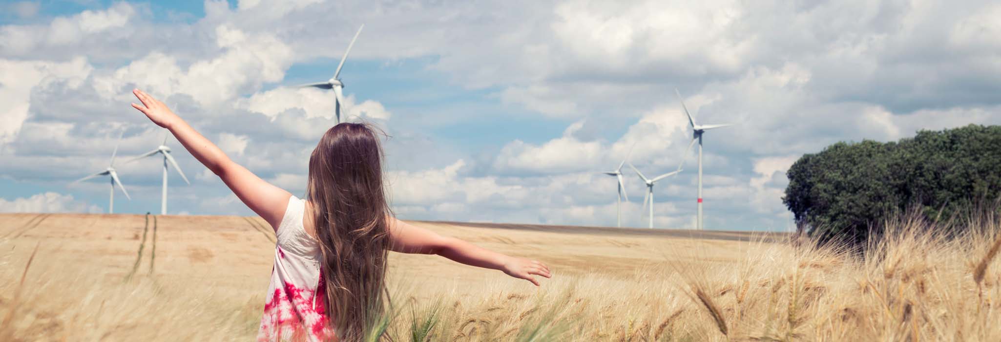 Young girl playing in field with wind turbines in the background.