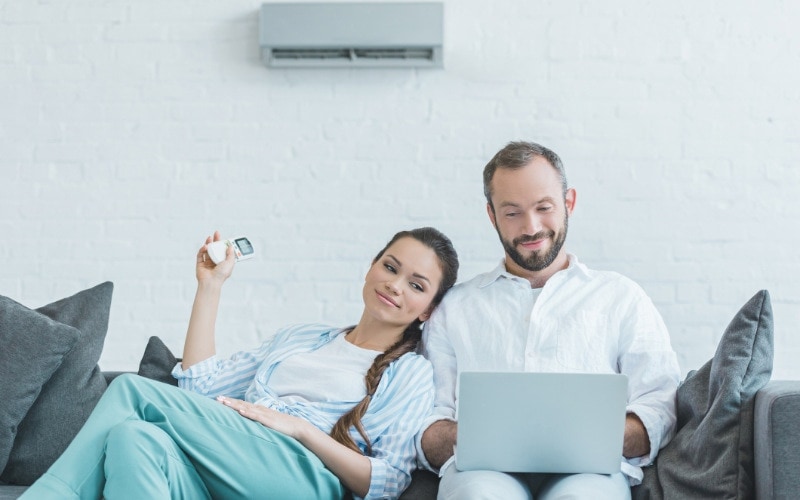 A woman and man cuddling on a couch under their AC unit.