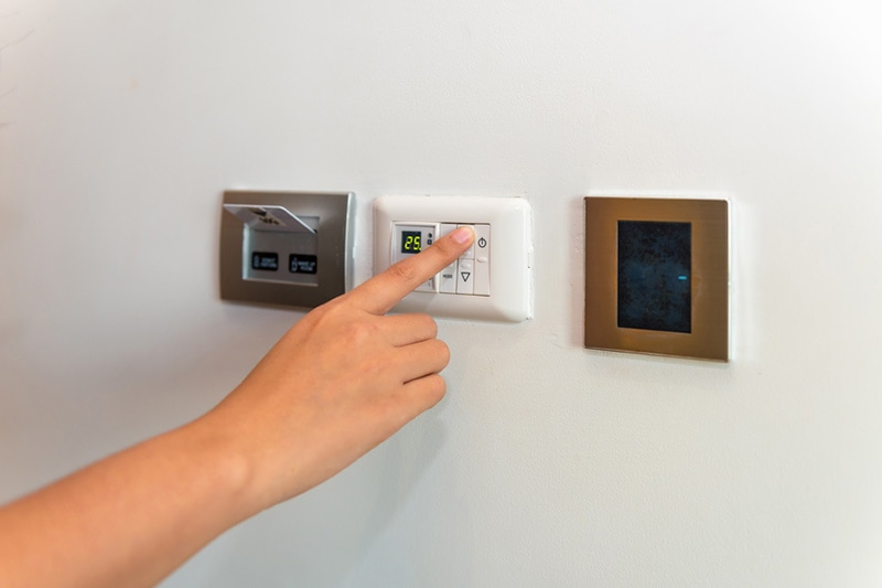 Homeowner adjusting temperature on thermostat.