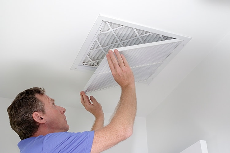 HVAC technician replacing air filter in ceiling.