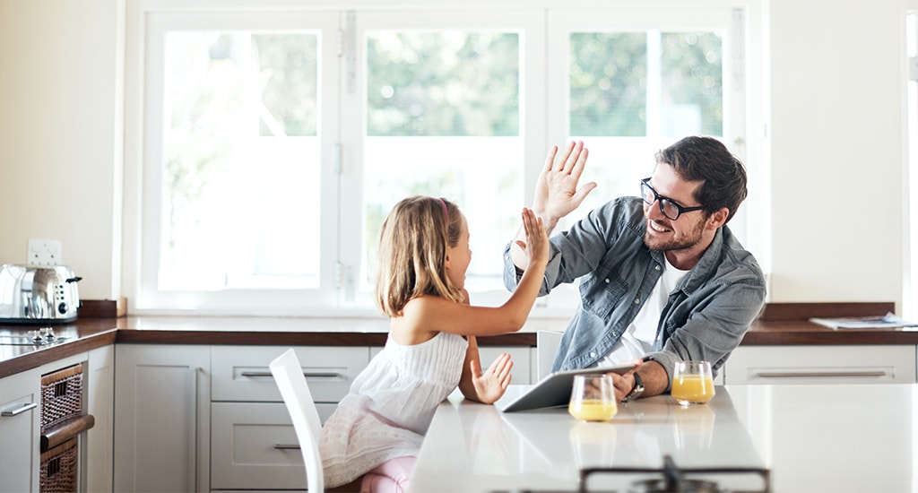 Dad high-fiving his daughter at kitchen table.