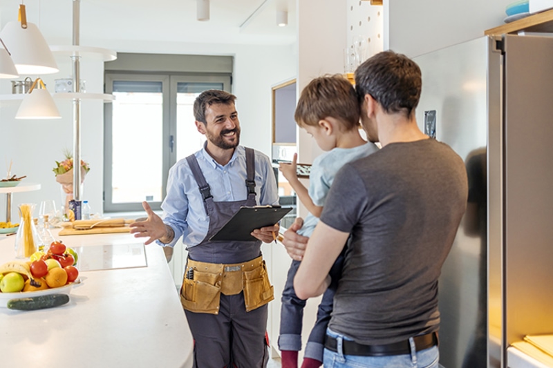 AC Maintenance Checklist - Professional plumber in uniform talking to male client and his small son indoors.