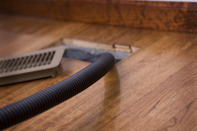 Air Duct Cleaning. Photo of a vacuum hose going inside an air duct for cleaning.