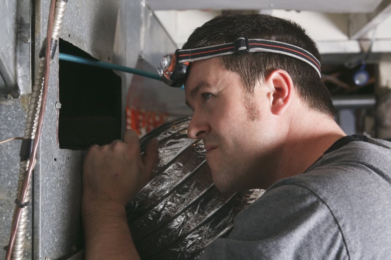 Why Is My Furnace Leaking Water? Professional inspecting a vent for water or dust.