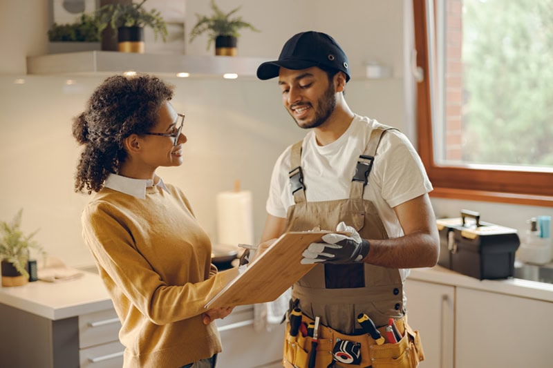 A friendly interaction between a service technician and a homeowner in a kitchen.