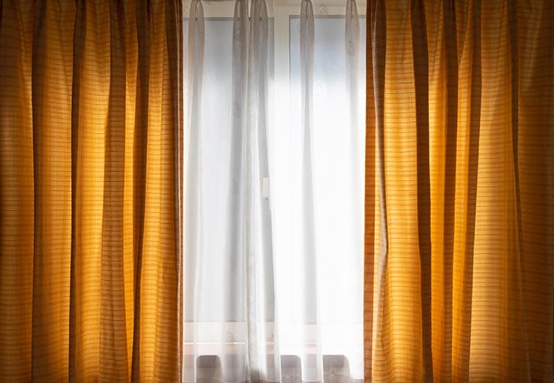 Soft, sheer white curtains hanging in front of a bright window, allowing diffuse natural daylight to filter into the room.